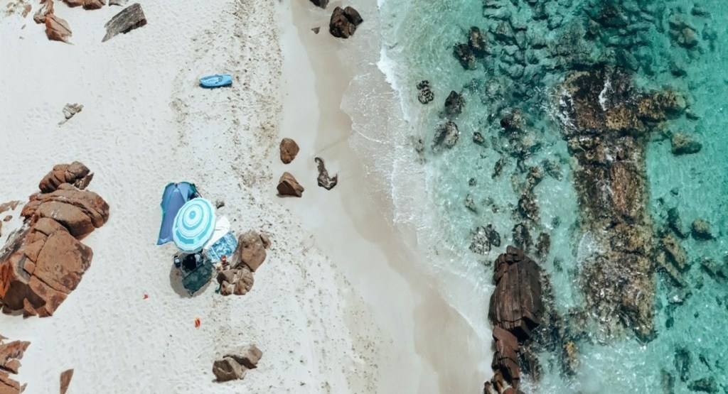 Aerial view of a family beach setup with an umbrella and a tent on a beach in Dunsborough