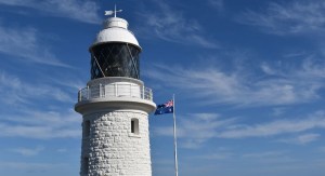 Cape Naturaliste lighthouse stands against a blue sky next to a waving Australian flag